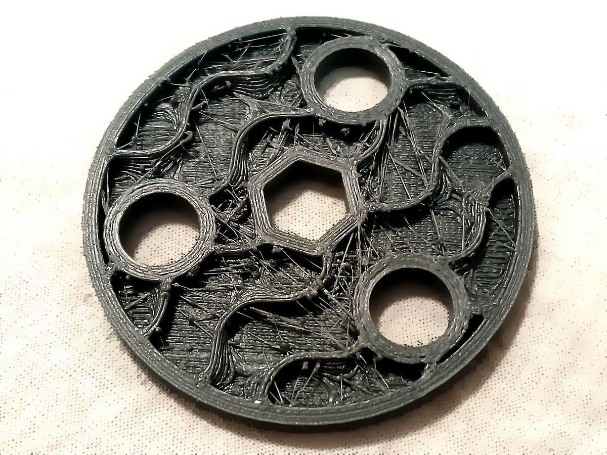 A dark grey 3D printed disc photographed from above with its top surface missing, showing two smooth outer wall loops around the rim and sparse curved infill lines inside