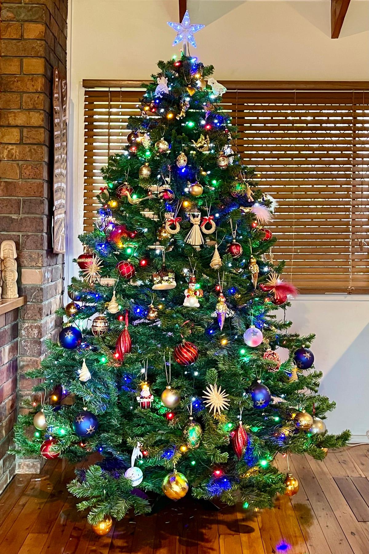 A fully decorated Christmas tree with coloured LED lights, glass baubles, straw stars and hanging figures