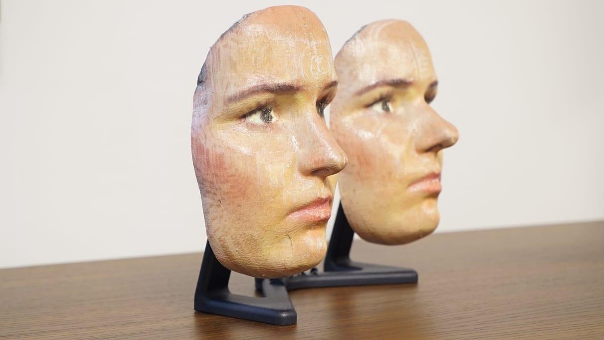 Two painted 3D printed face masks mounted on small stands on a desk, with print layer texture still visible through the paint