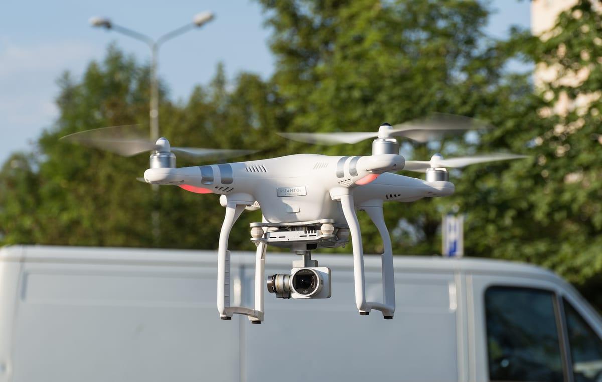 A white DJI Phantom 3 quadcopter photographed from the side, showing its four arms, landing legs and gimbal-mounted camera