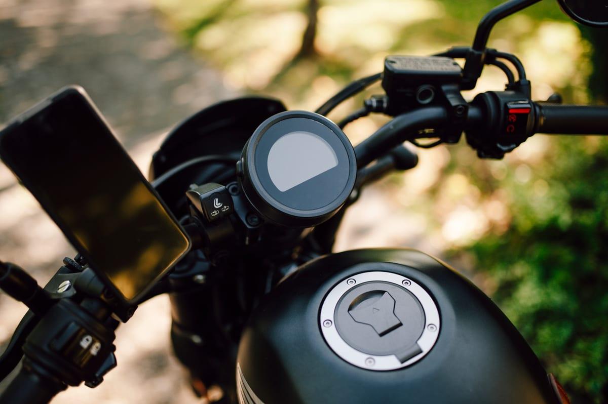 Motorcycle dashboard and handlebar with a round instrument display and a smartphone holder mounted alongside