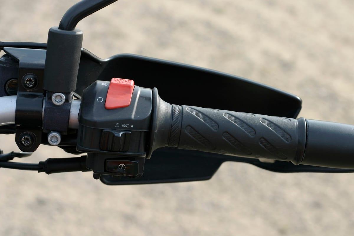 Right-hand handlebar of a BMW F650 in close-up, showing the switch housing with a red engine stop switch, a starter button and a light switch, next to the throttle grip and a hand guard