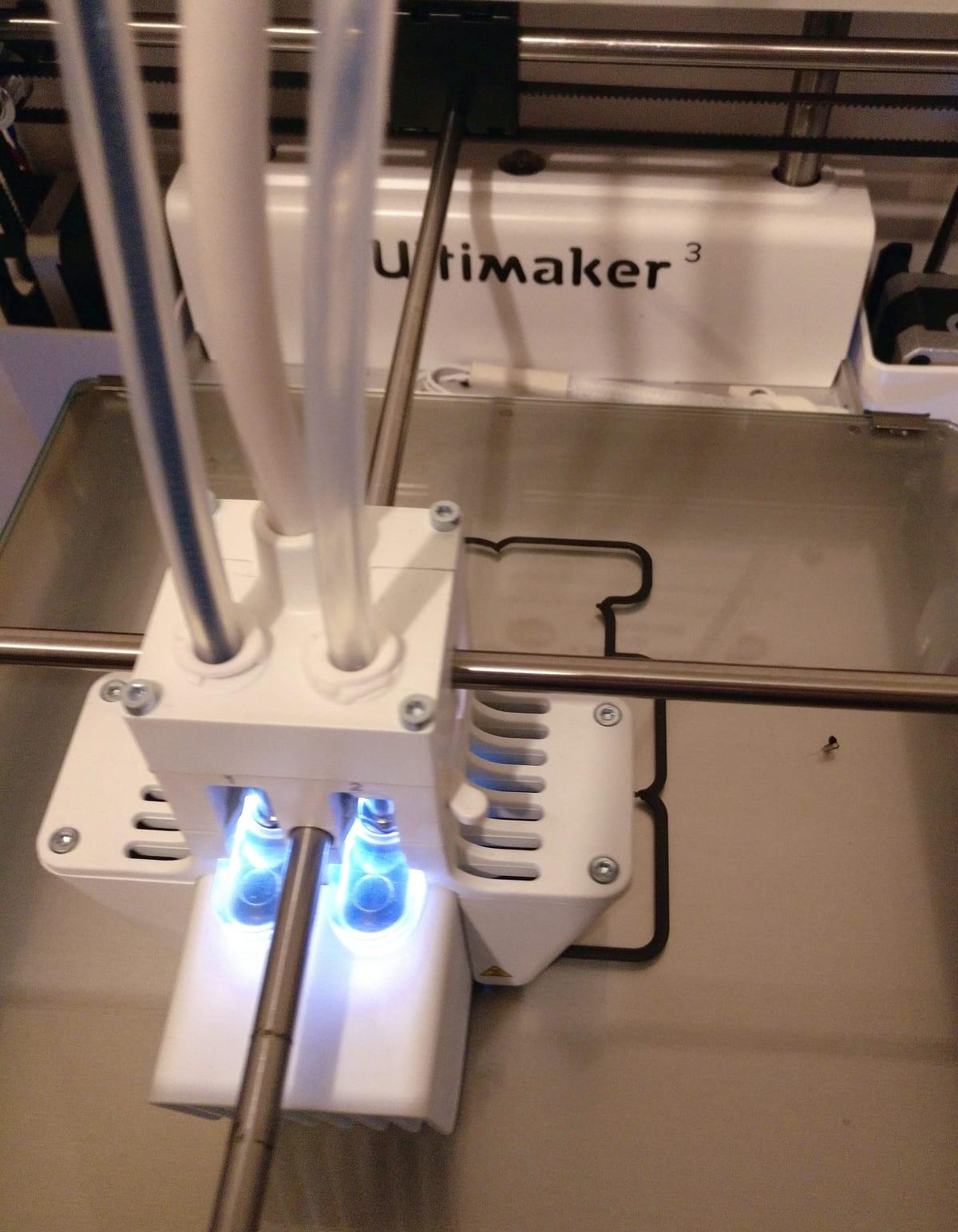 Close-up of a dual-nozzle FDM printer toolhead moving above a build plate during a print