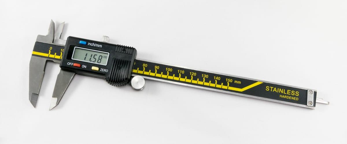 A black and yellow stainless digital caliper lying on a plain white background, its LCD reading 11.58 mm