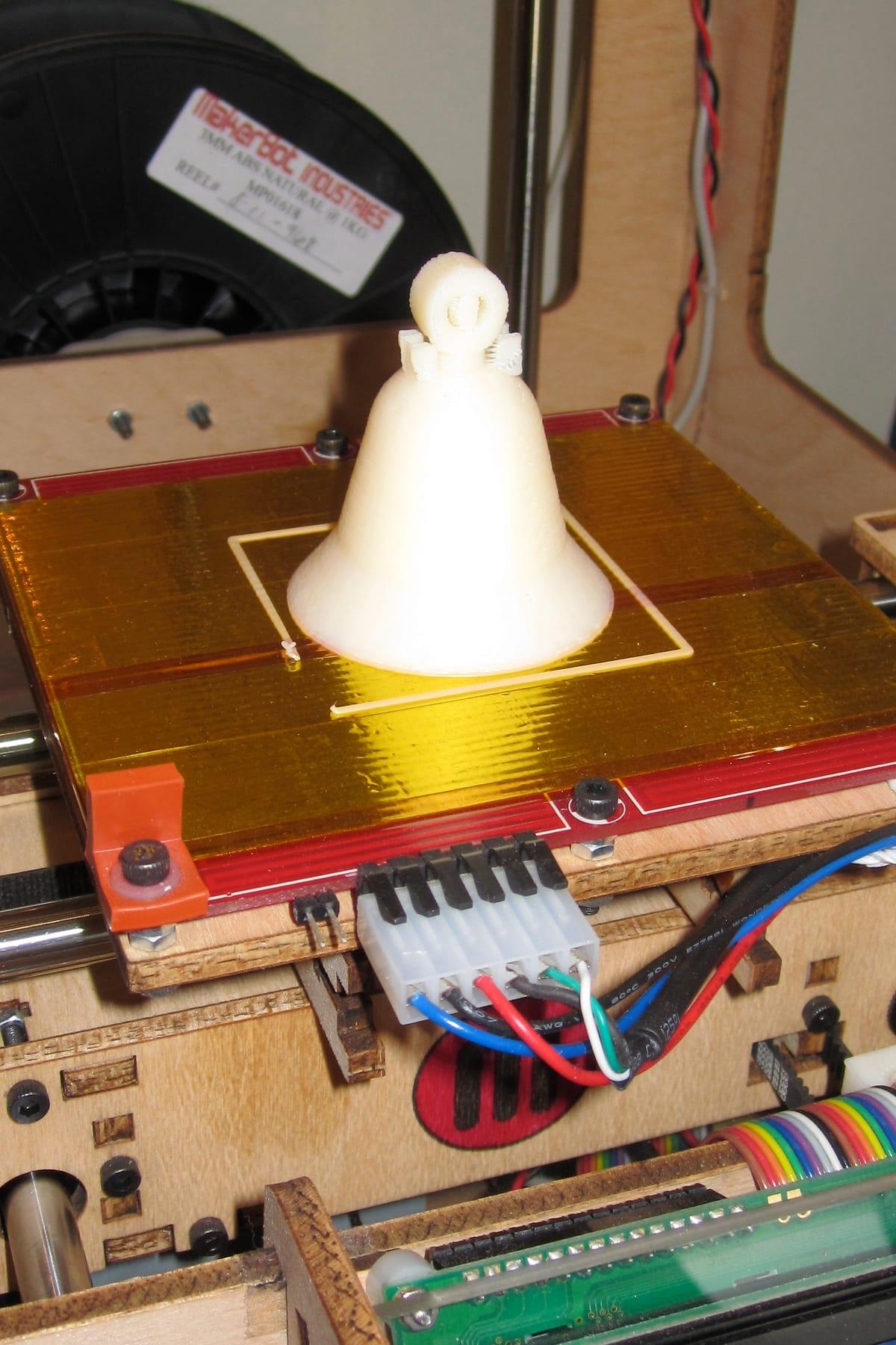 A bell-shaped object 3D printed in ABS filament, still attached to the printer bed