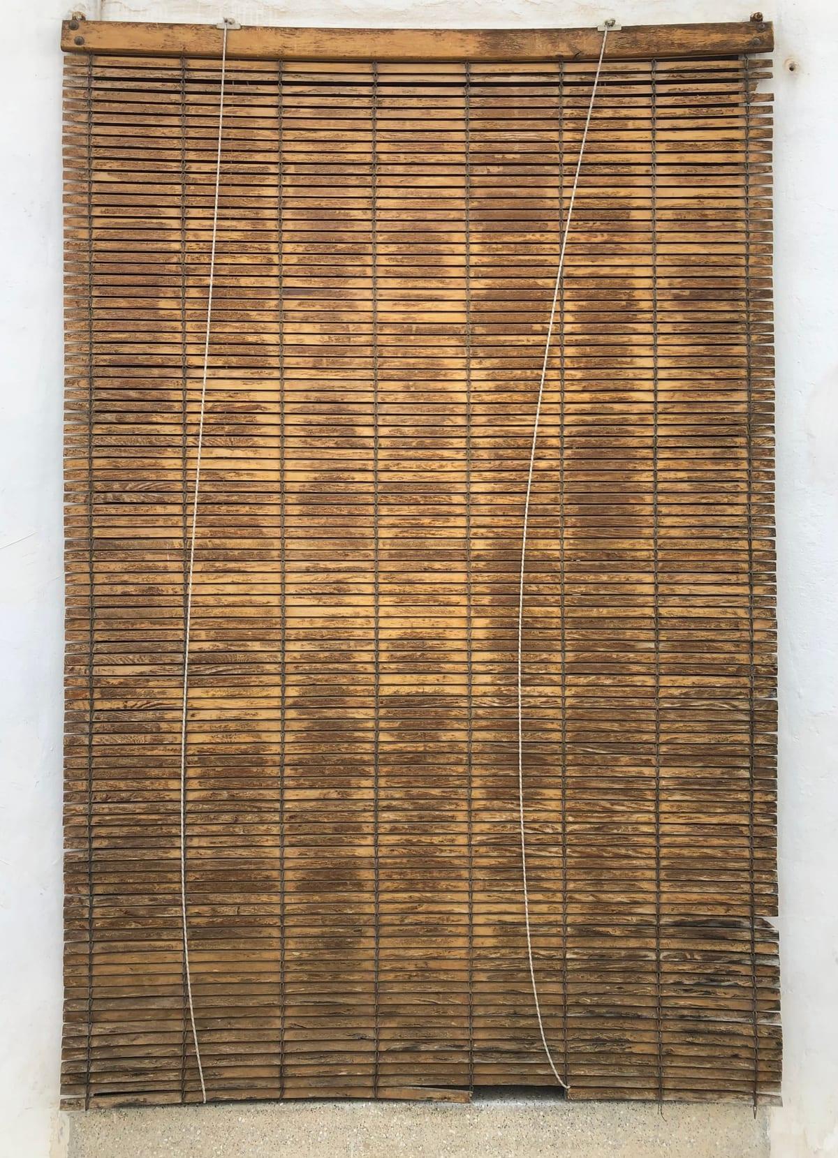 Weathered wooden roll-up matchstick blind hanging on a whitewashed wall with two lift cords running down it