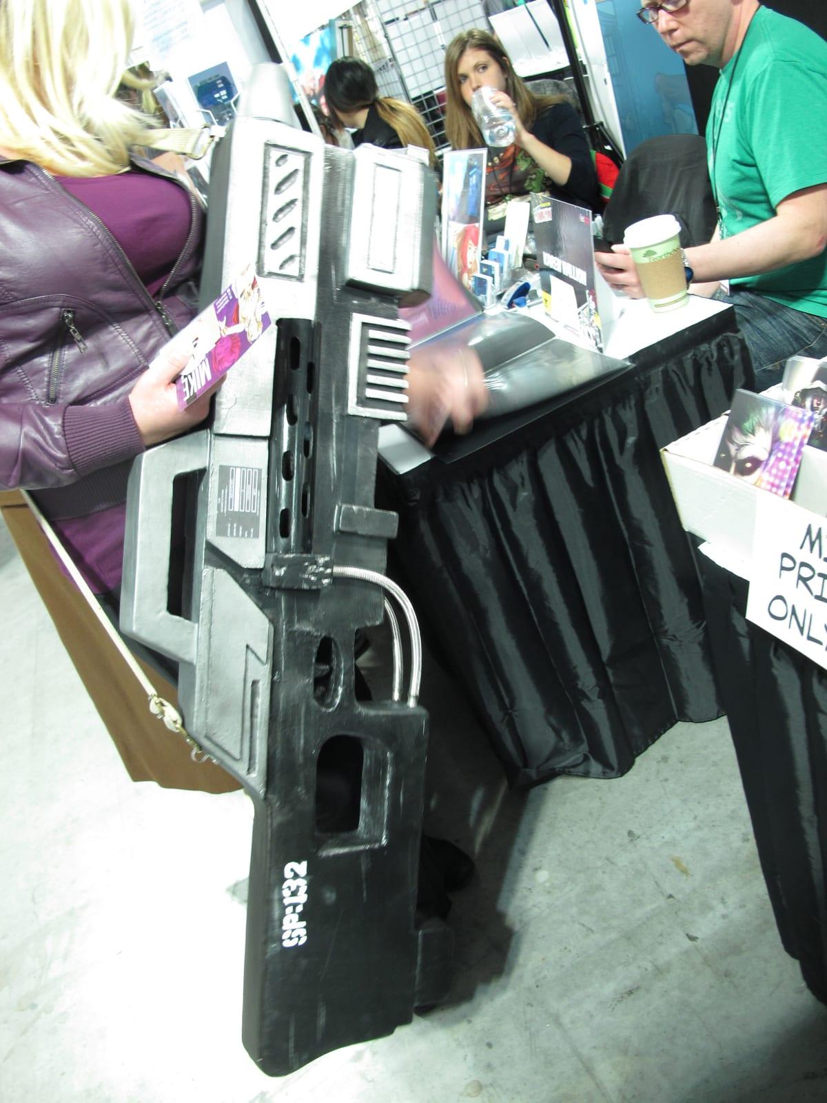 Close-up of a large handmade prop weapon carried by a cosplayer at a comic convention, showing painted surface detail and weathering