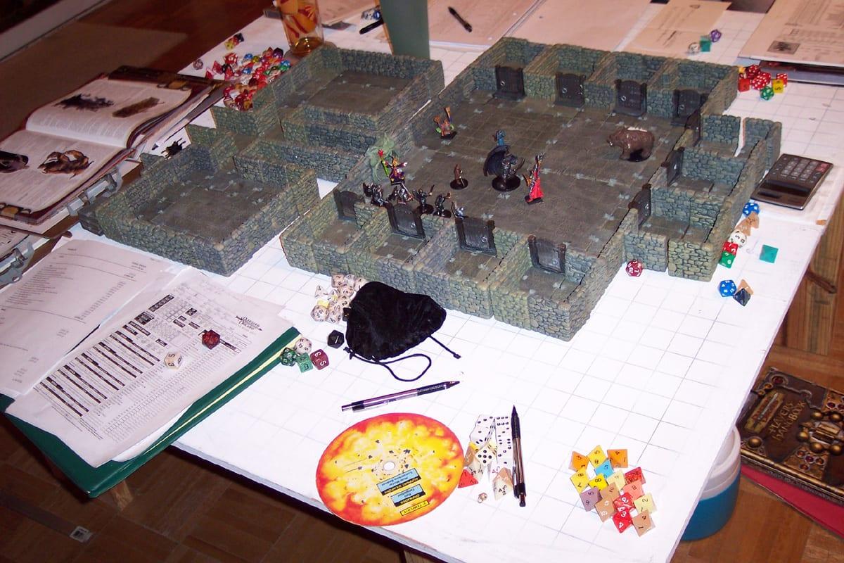A tabletop role-playing game in progress with miniatures placed on modular dungeon scenery, dice and a character sheet visible