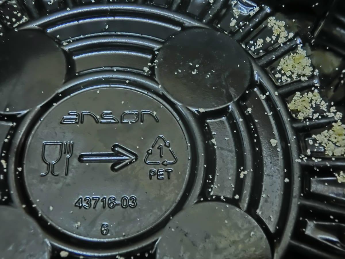 Close-up of a black plastic food container showing a moulded recycling triangle with the number 1 and the letters PET