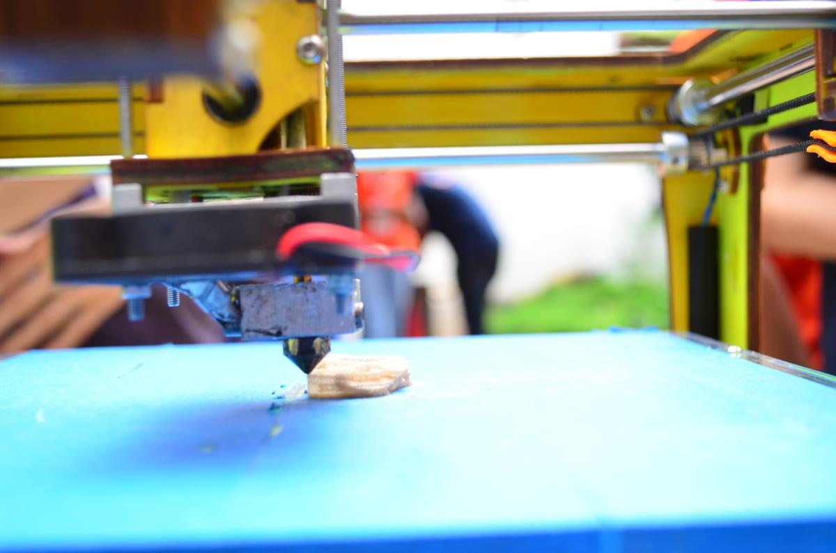 Desktop 3D printer mid-print, with the nozzle laying down filament on a partially finished part