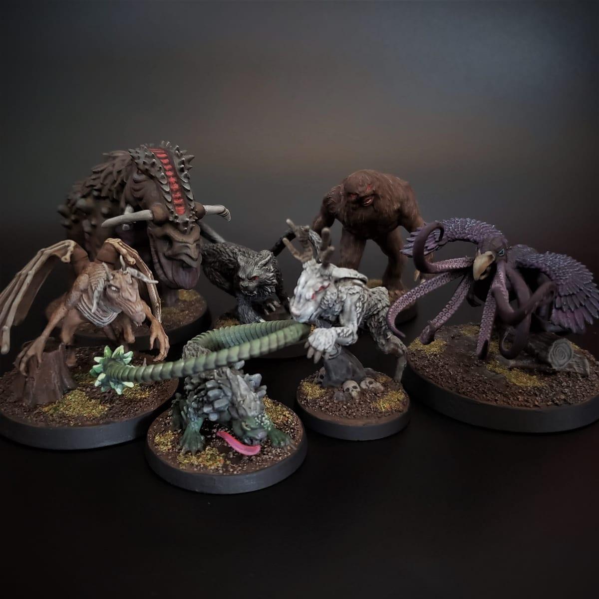 Seven painted tabletop miniatures of creatures on round bases, photographed against a dark background