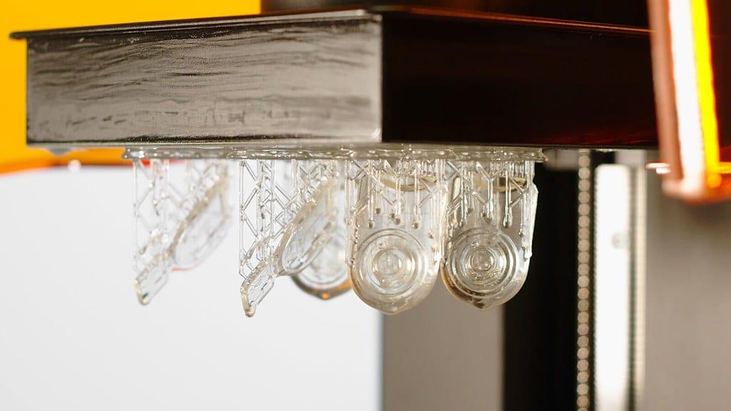 Clear resin parts hanging from a 3D printer build platform on a lattice of supports