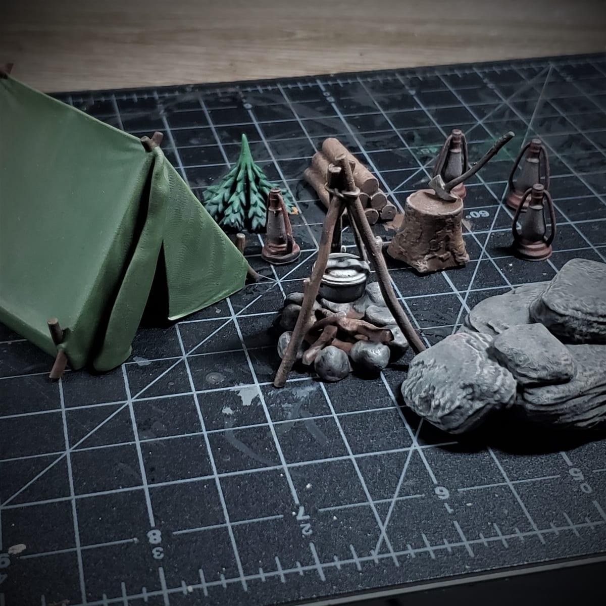A group of small 3D printed tabletop miniatures depicting a campsite, hand painted in multiple colours with shading and highlights
