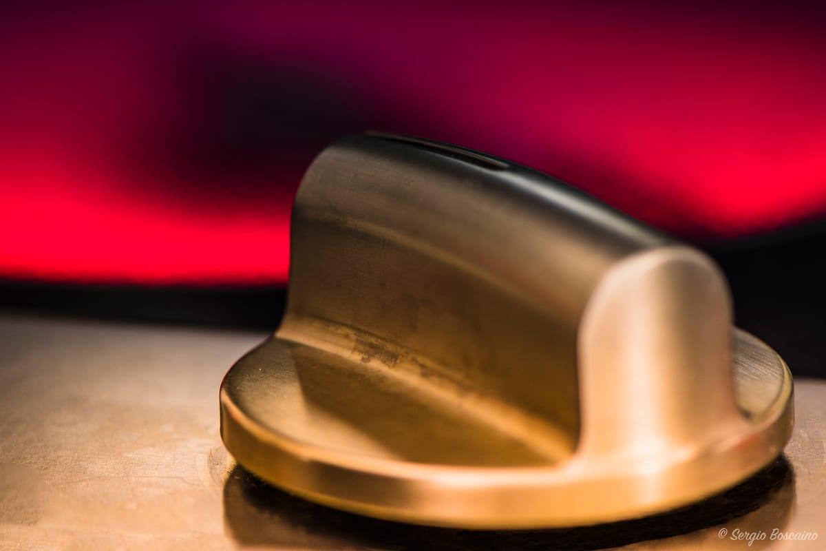 Extreme macro close-up of a single cooker control knob, showing its metallic-finished body, dark top face and pale pointer against a red background