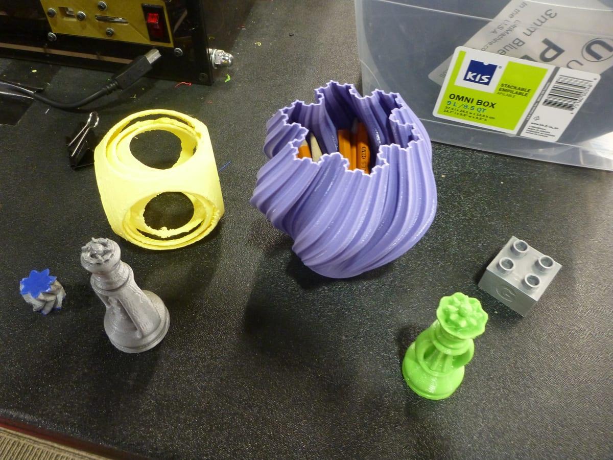 Finished 3D printed sample parts on a workbench beside a printer