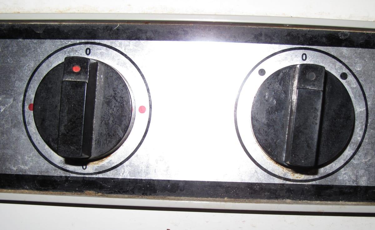 Two worn black rotary control knobs on an old washing machine panel